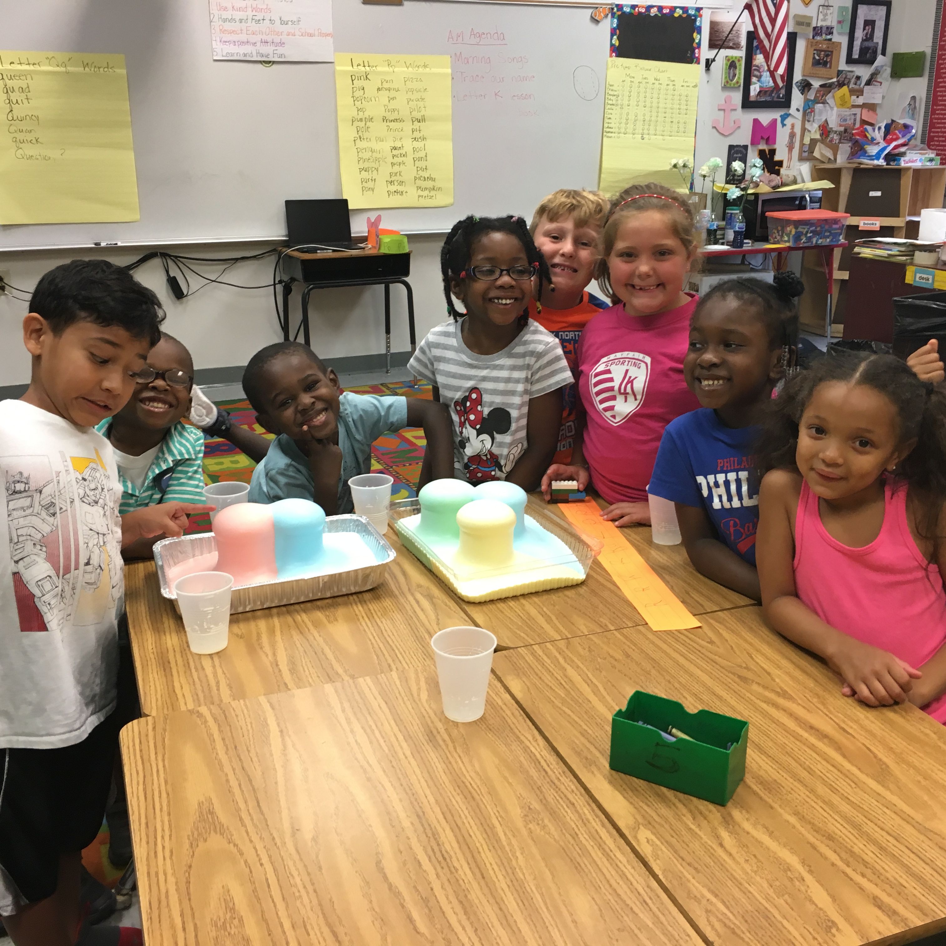 Several young students smiling at a table with colorful foaming cups