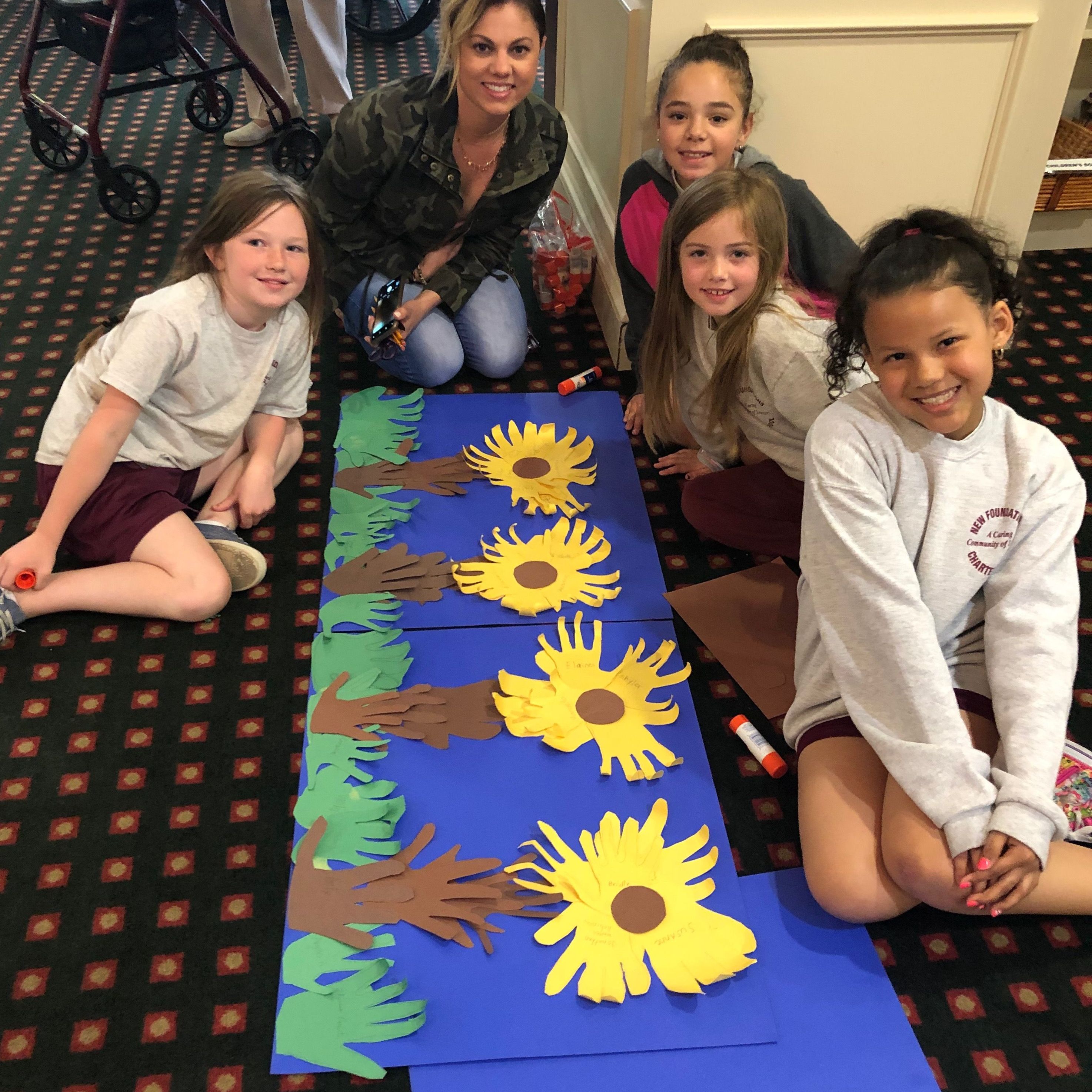 4 young female students and a female teacher pose around artwork of sunflowers